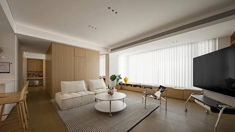 Modern minimalist living room with white couches and wooden furniture, featuring a round coffee table and large windows.