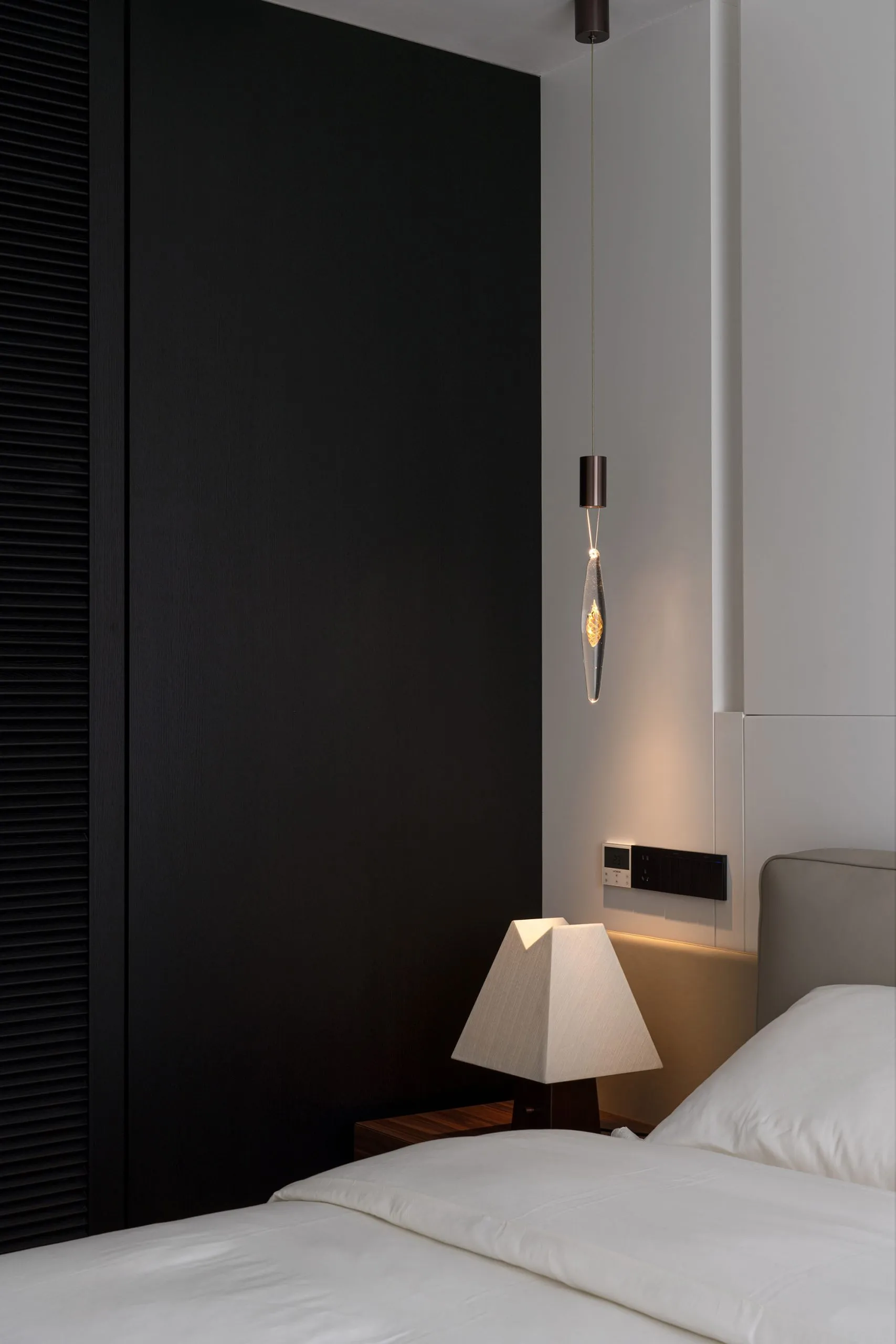 A minimalist bedroom with black and white color scheme featuring a modern lamp and a light fixture with a unique design.