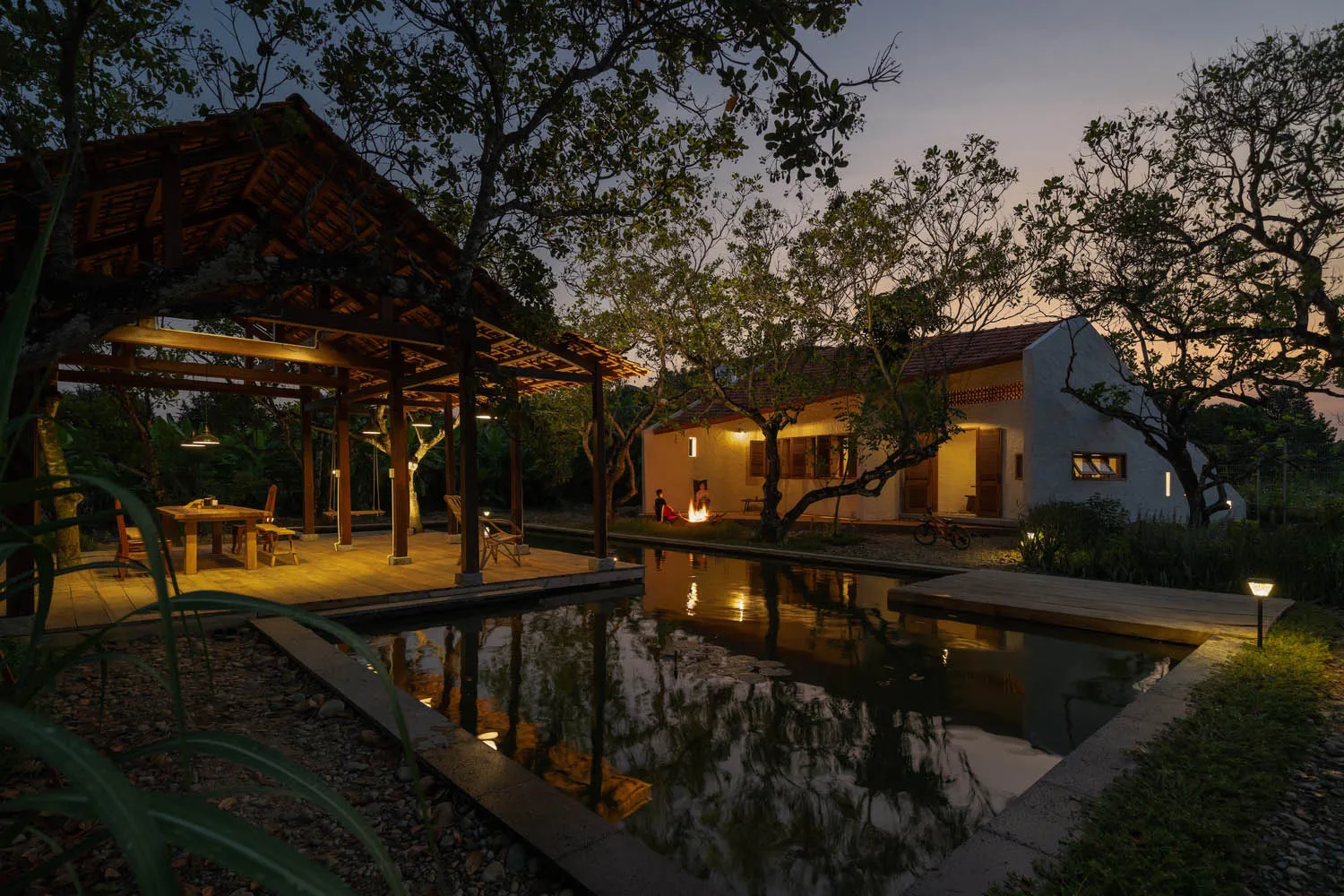 Modern house exterior with wooden pergola, brick walls, stone patio, and water feature during evening time.