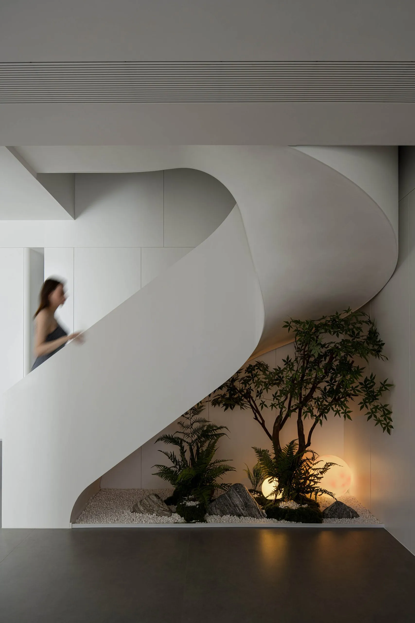 A modern interior featuring a white concrete staircase with a small garden at the bottom.