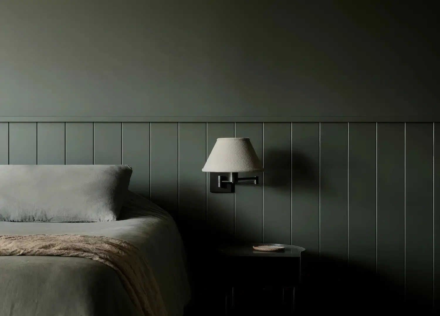 A minimalist bedroom with wooden walls and a comfortable bed, featuring a simple bedside lamp and a small table.