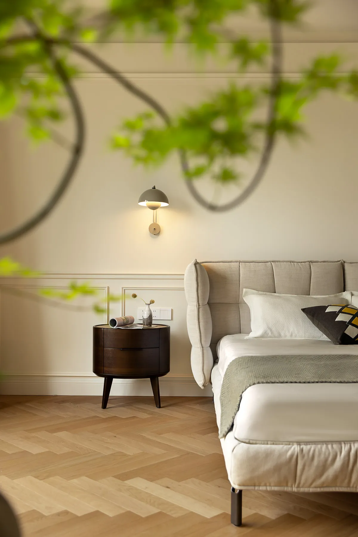 A modern minimalist bedroom featuring a beige upholstered bed with a wooden bedside table and a sleek, wall-mounted lamp.