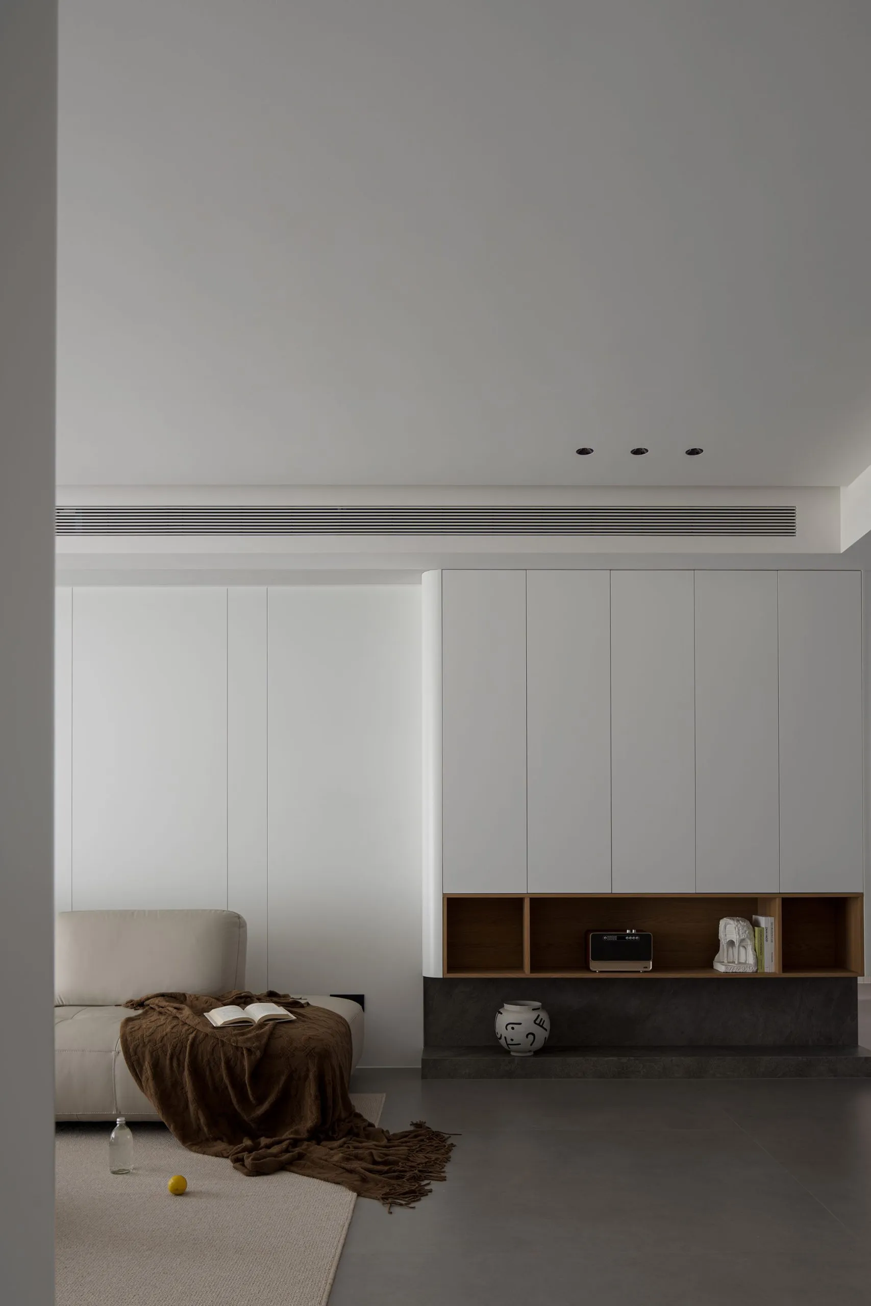 A minimalist living room featuring concrete walls and a white leather couch, with a modern cabinet and sleek lighting.