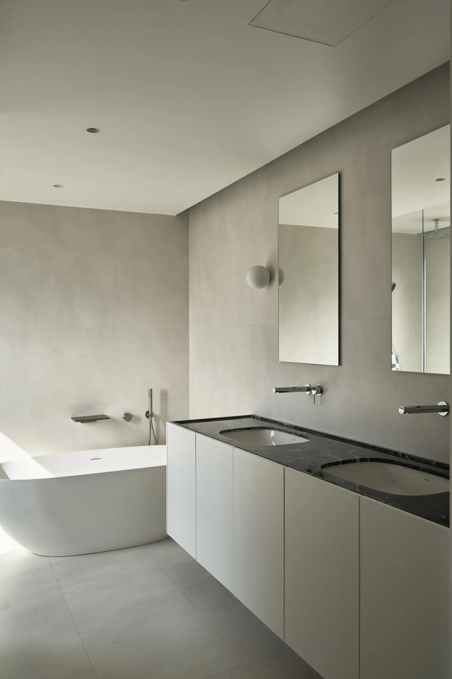 A modern minimalist bathroom featuring a freestanding bathtub made of white marble and a white vanity with black marble count