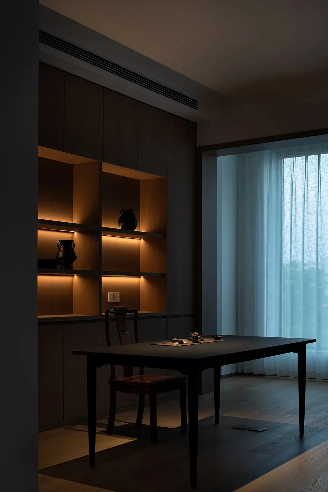 A modern dining room featuring wooden shelves and a dark wood table with a tea set.