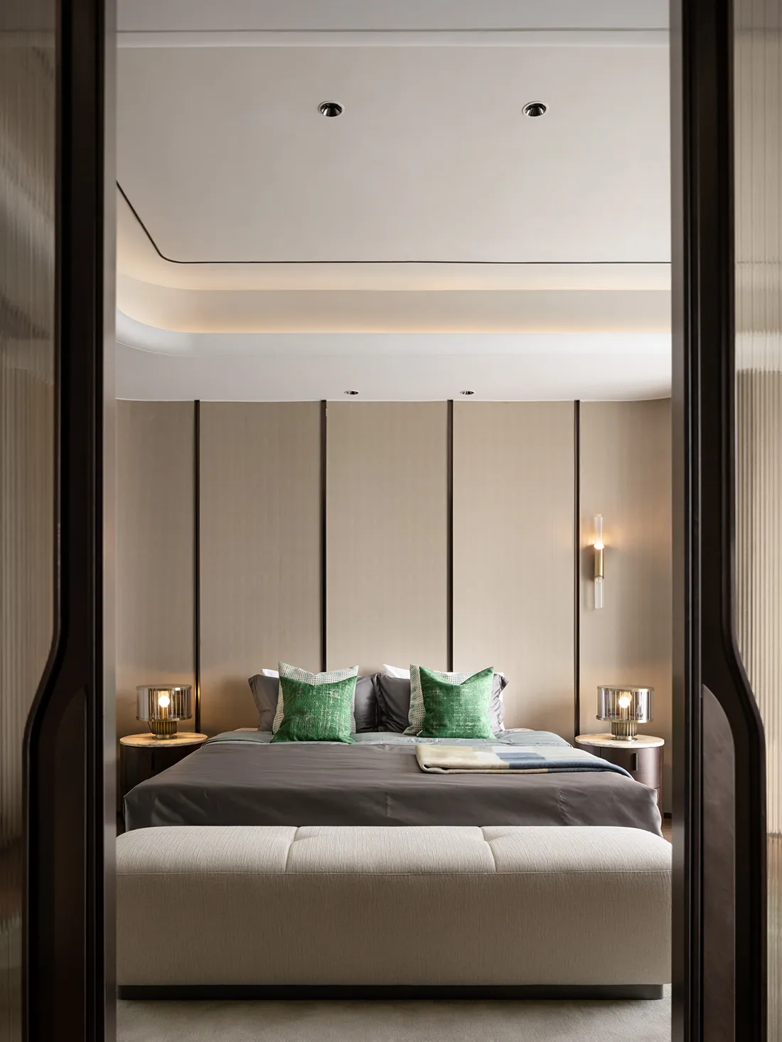 A minimalist bedroom featuring textured fabric on the bed, wooden headboard, and glass bedside lamps.