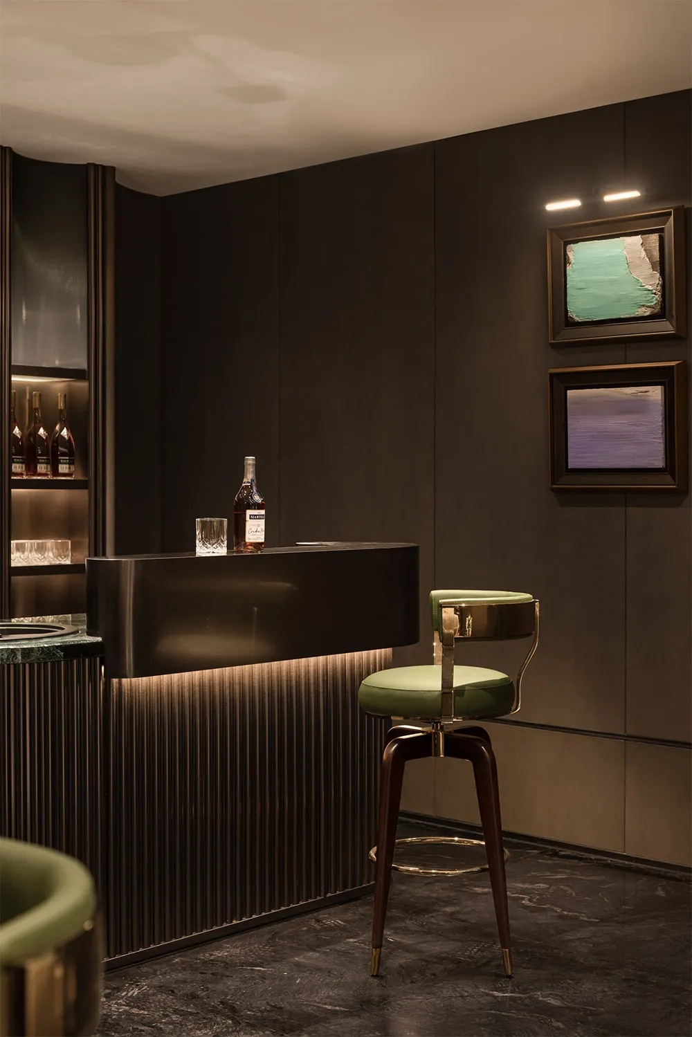 Modern bar with a marble counter, green stools, and framed abstract art in dark interior design space.