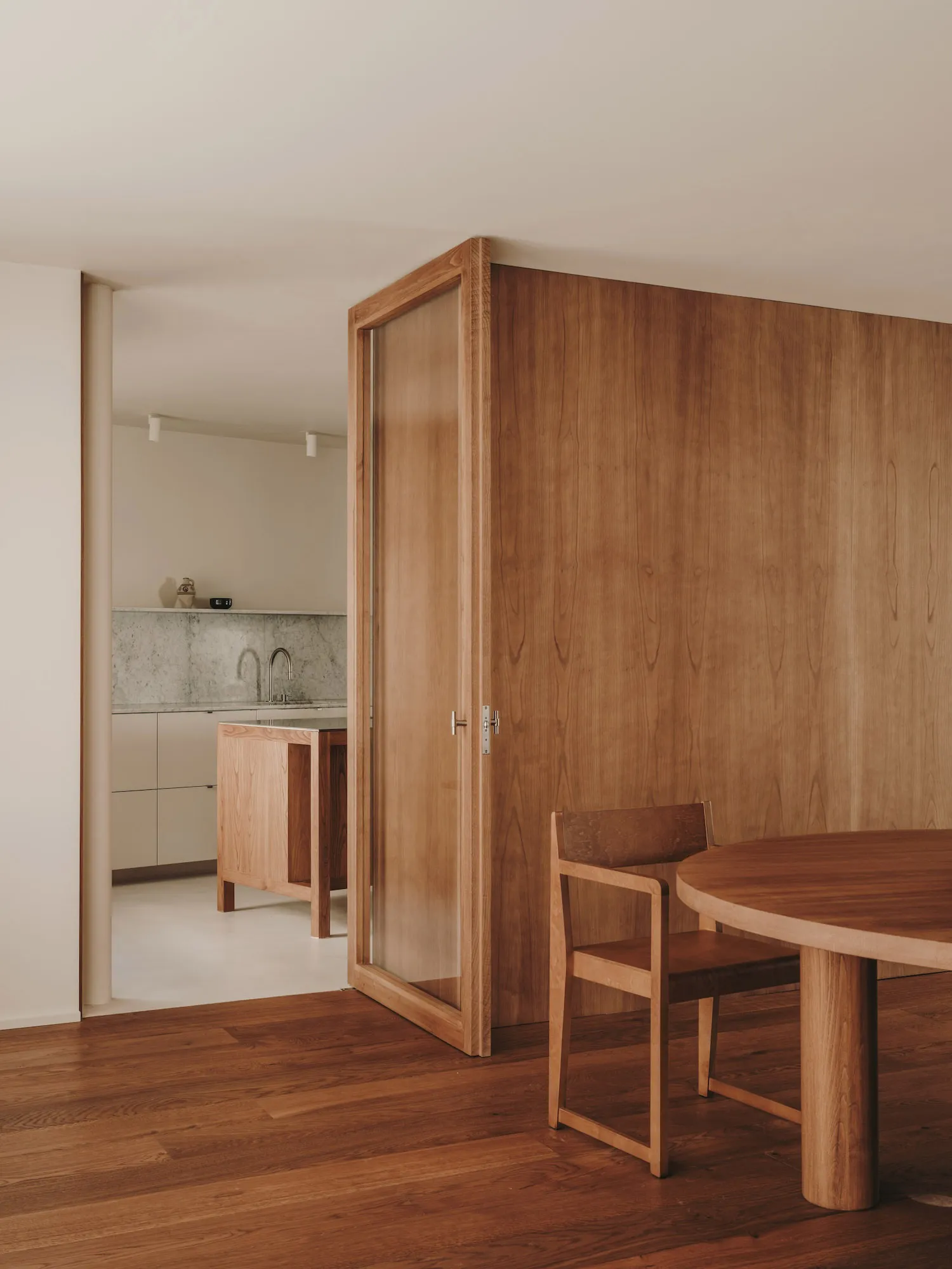 A modern dining space with wooden furniture and a kitchen area in the background.