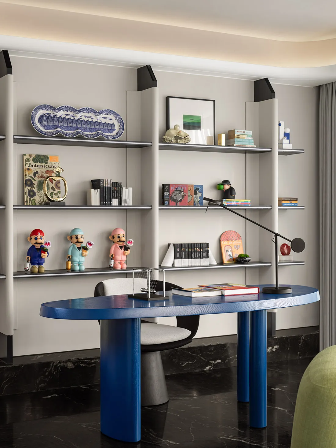 A minimalist home office featuring a blue desk and marble shelving with various decorative items and books.
