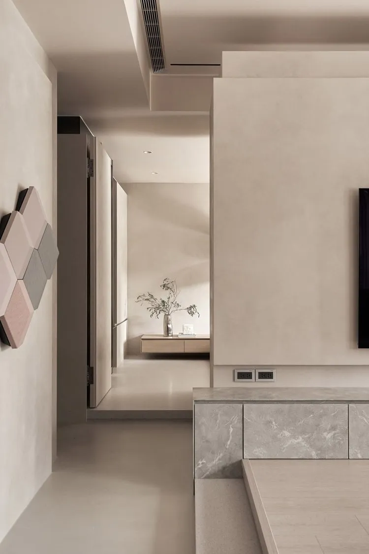 A minimalist living room with concrete walls and floor, featuring a wall-mounted TV and a floating shelf.