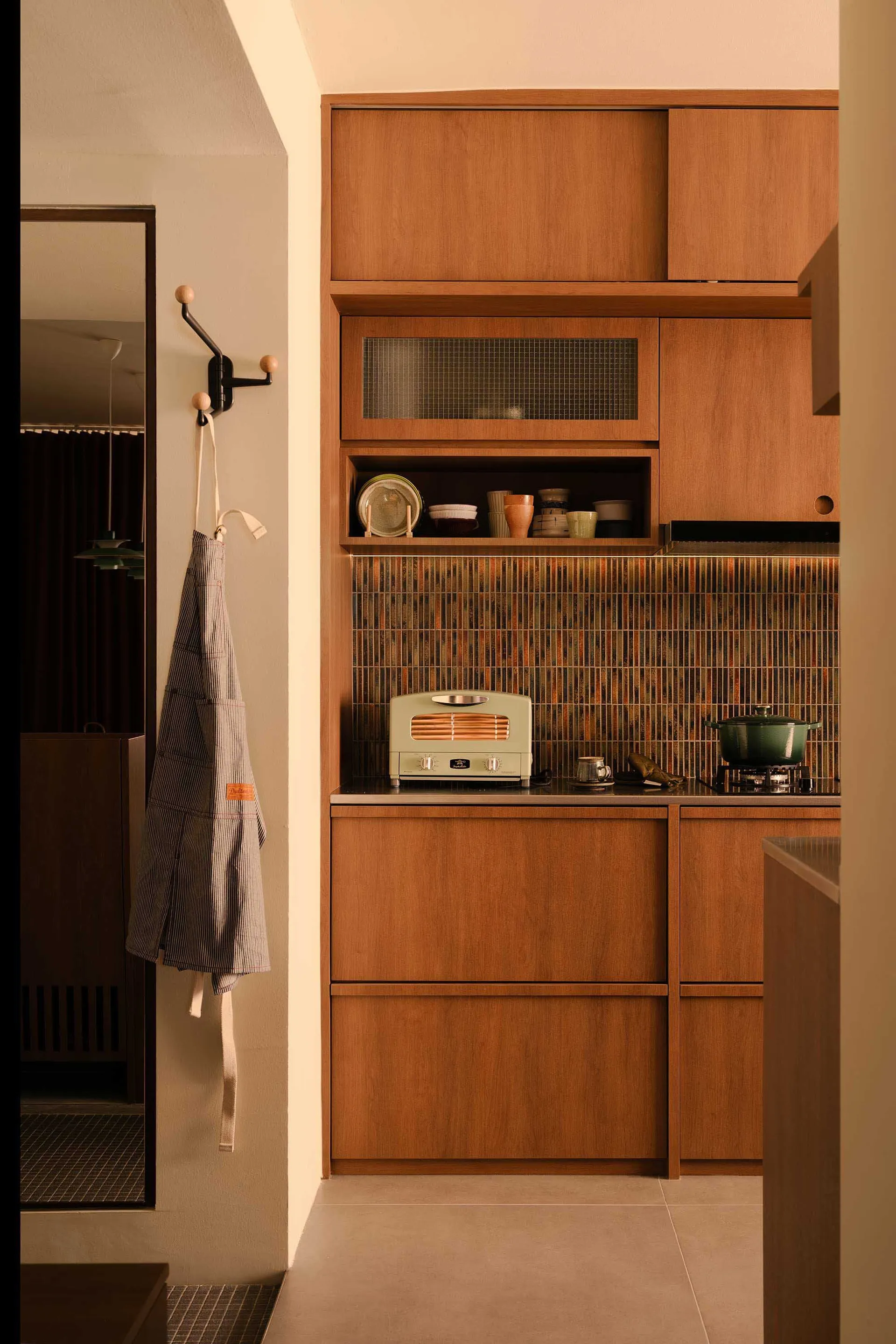 A modern minimalist residential kitchen featuring wooden cabinets and glass mosaic tiles.