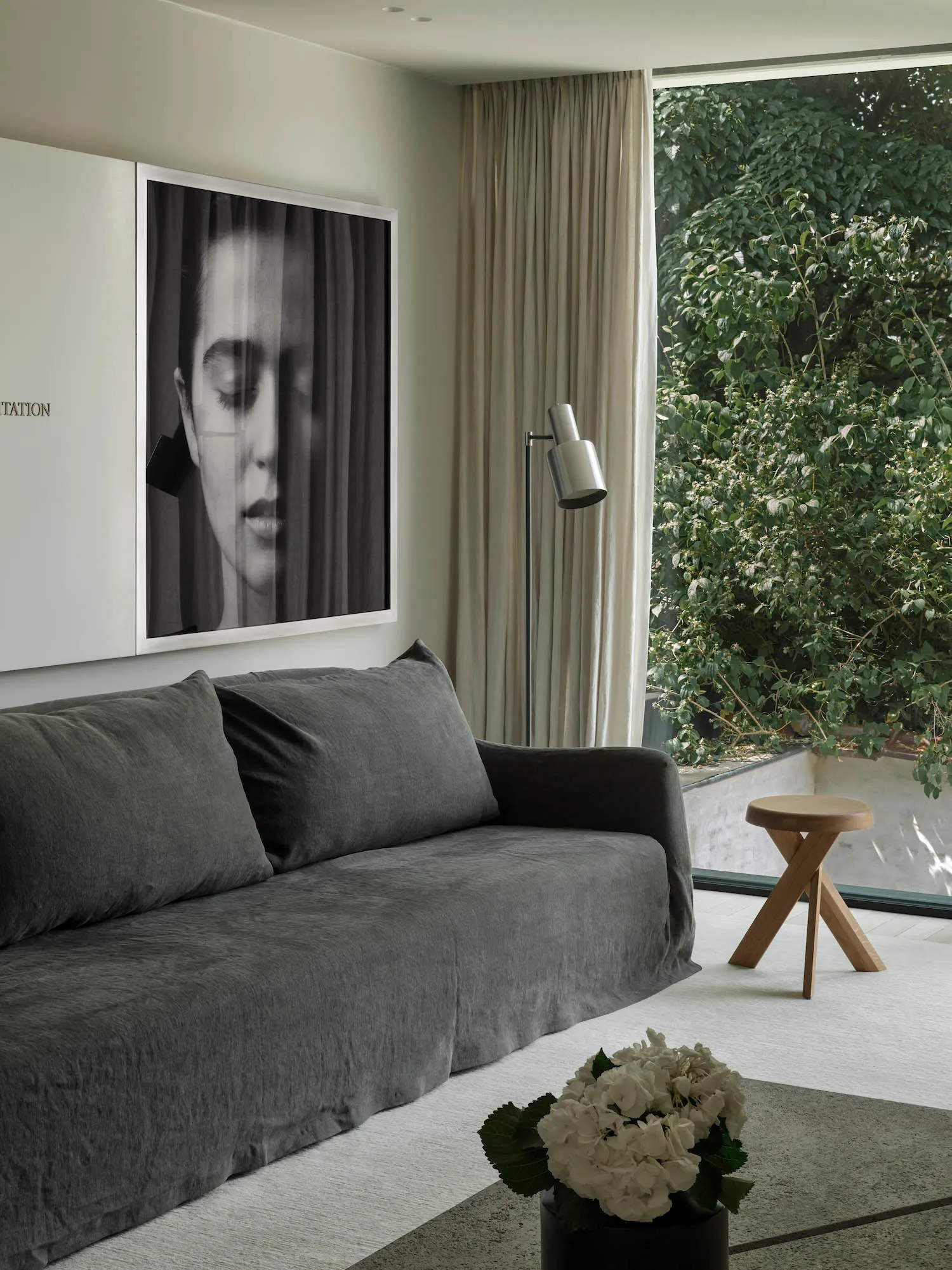 A modern interior design featuring a grey sofa, white curtains, and a minimalist lamp.