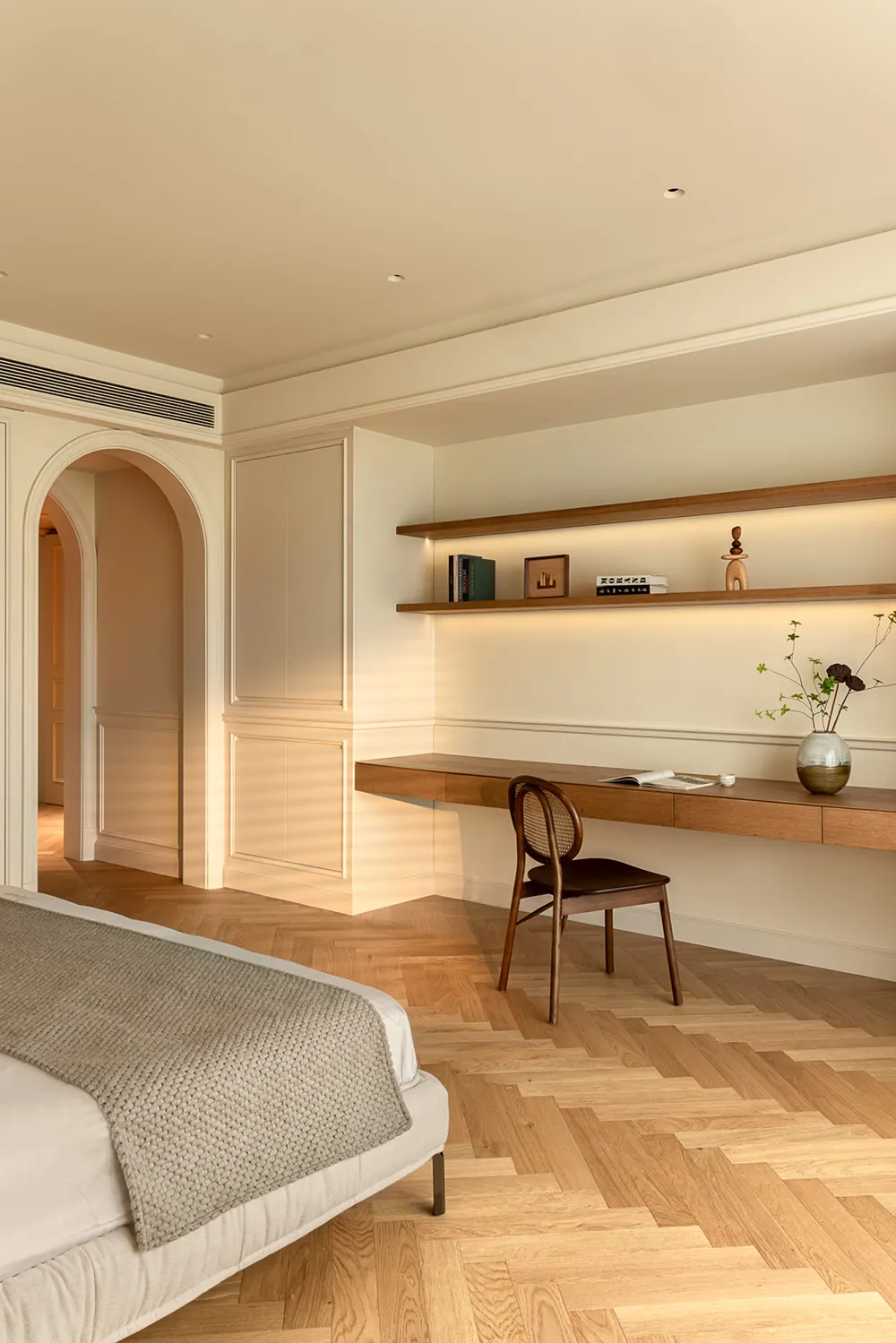 Minimalist bedroom with beige walls, wooden floor, and a desk with shelves.