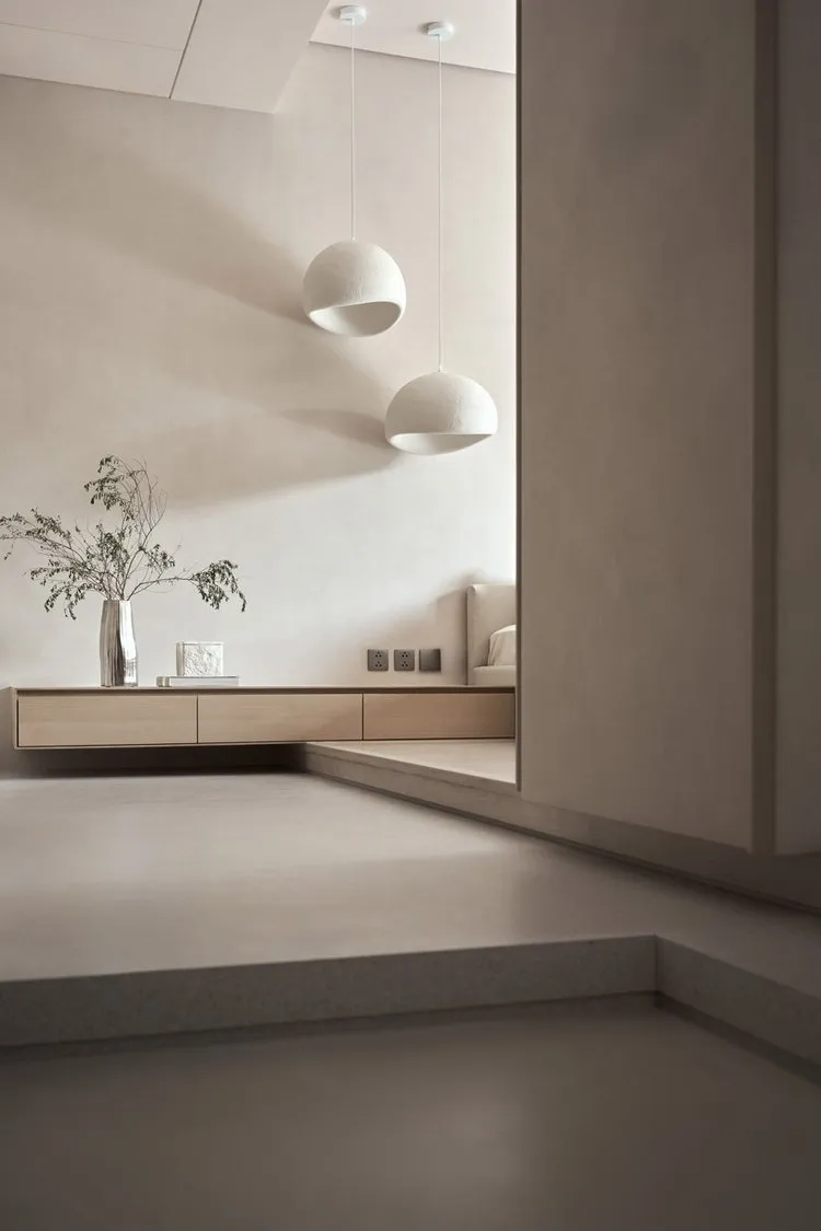 A minimalist living room featuring concrete walls and flooring, with two spherical pendant lights hanging above.