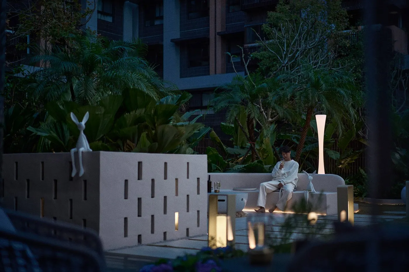 A minimalist living room with a concrete element as the centerpiece, surrounded by lush greenery and modern furniture.