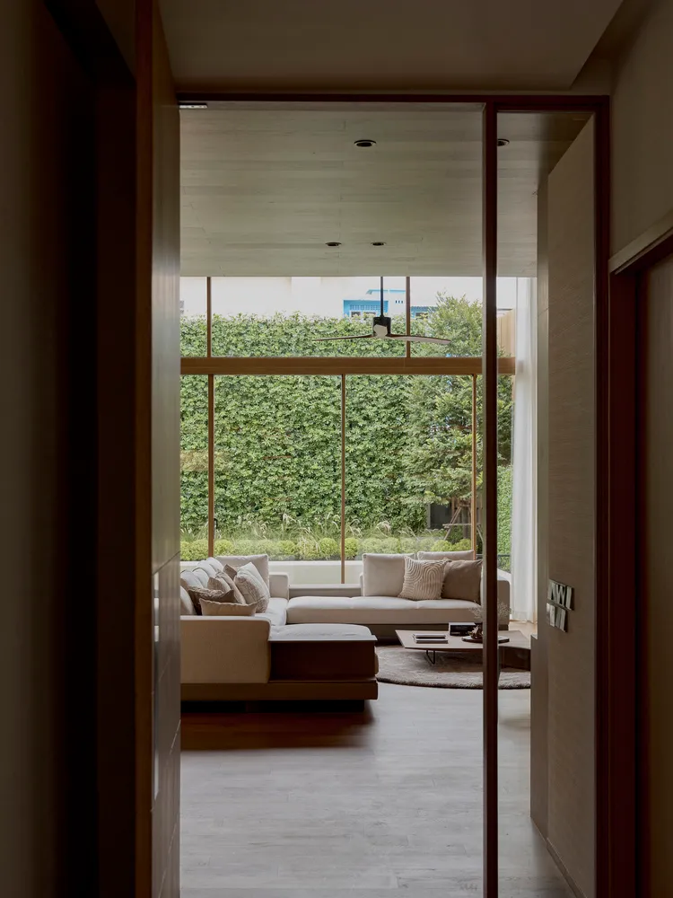 Modern cozy living room with a textured sofa and large windows overlooking a green outdoor area.