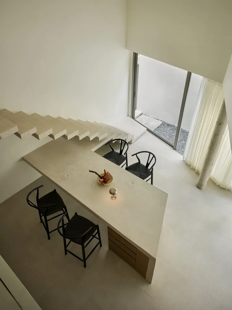A modern kitchen with a concrete countertop, black chairs, and a bowl of fruit.