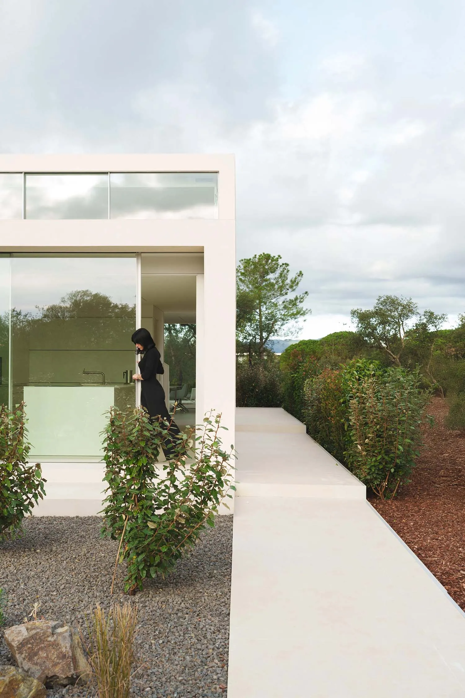 Modern residential exterior with large glass windows and a white concrete pathway.