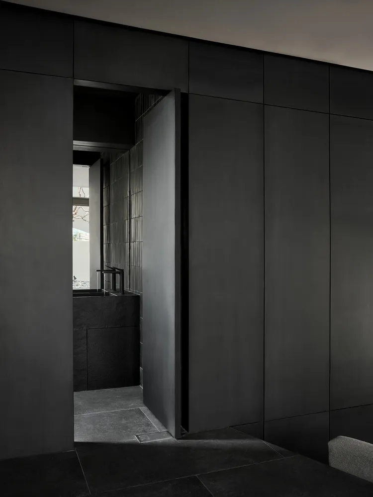 Modern minimalist bathroom with black walls and concrete tiles, featuring a sleek sink and small window.
