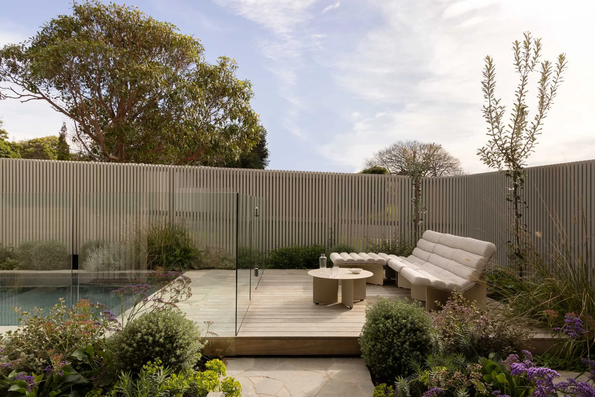 Modern patio featuring wood deck, glass barrier, and greenery.