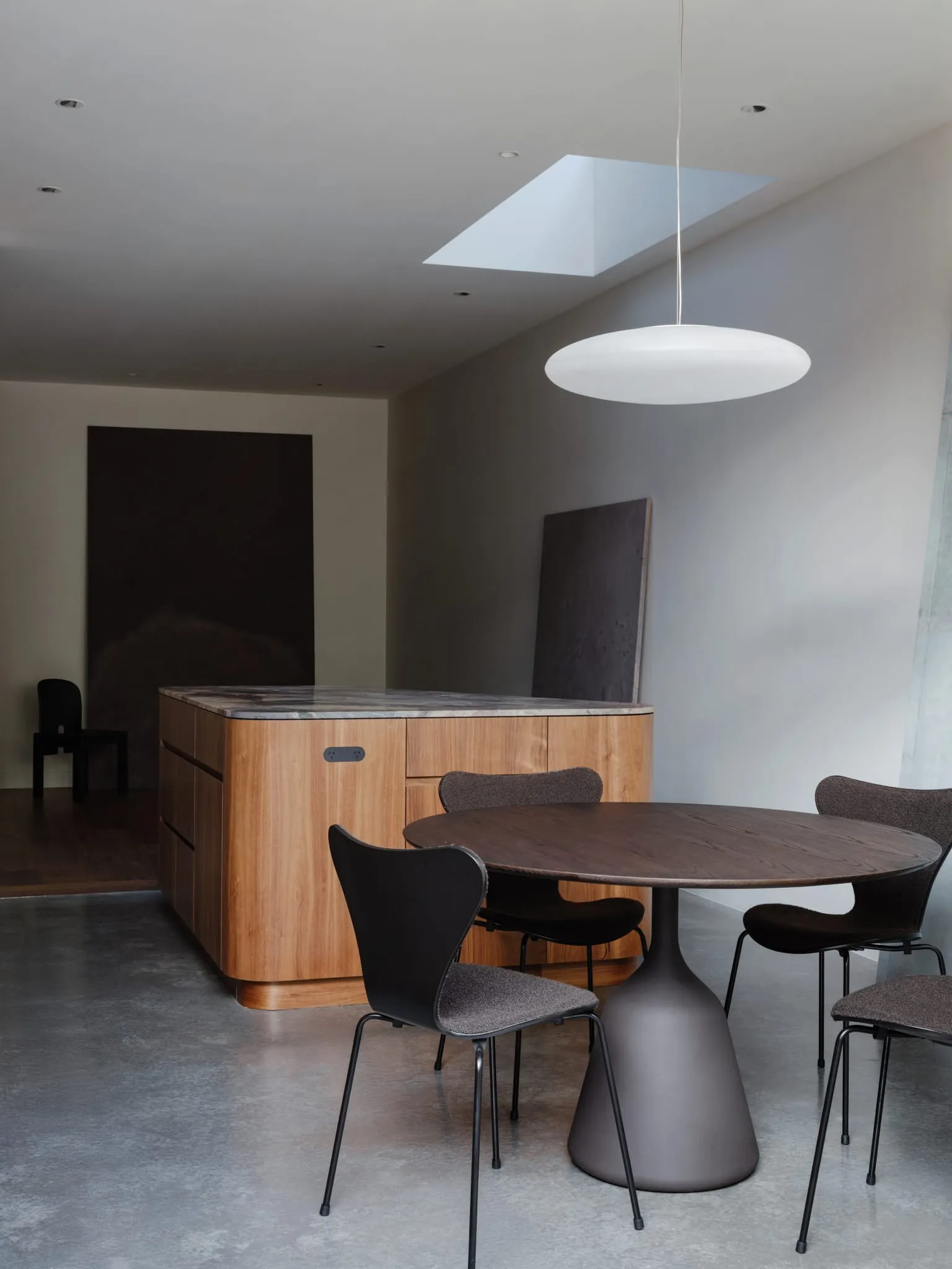 Modern kitchen with wooden dining table, marble countertop, concrete floor, and hanging lamp.
