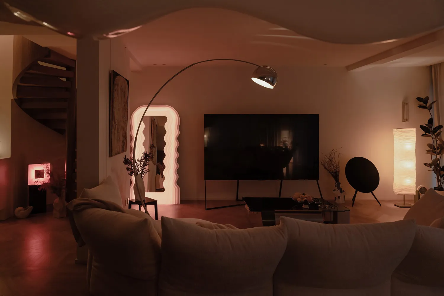 Modern living room with minimalist decor, featuring a curved floor lamp, a television, and comfortable seating.