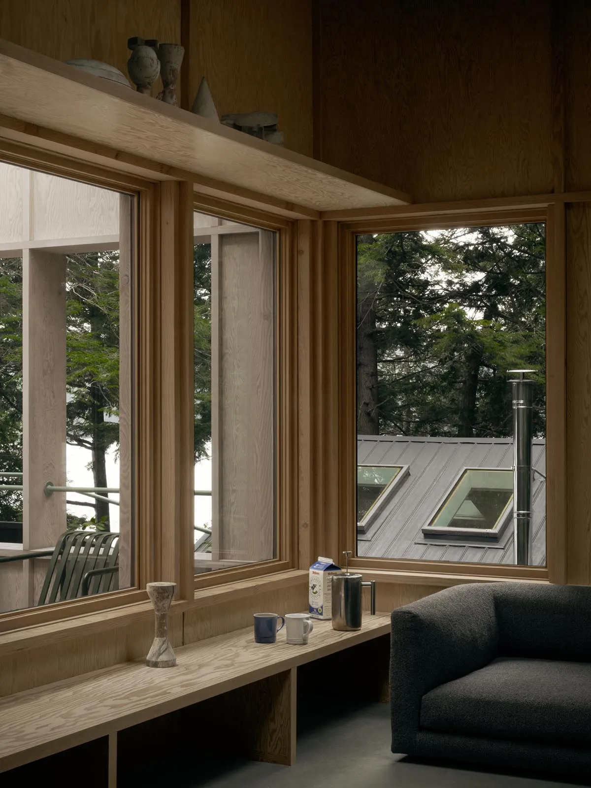 A modern living room featuring a wooden window sill with a view of trees outside and a grey armchair.