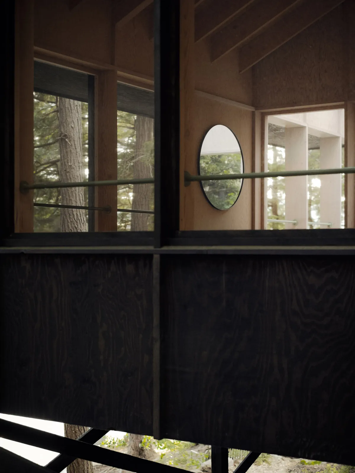 A modern treehouse interior with wooden panels, large windows, and a circular mirror.
