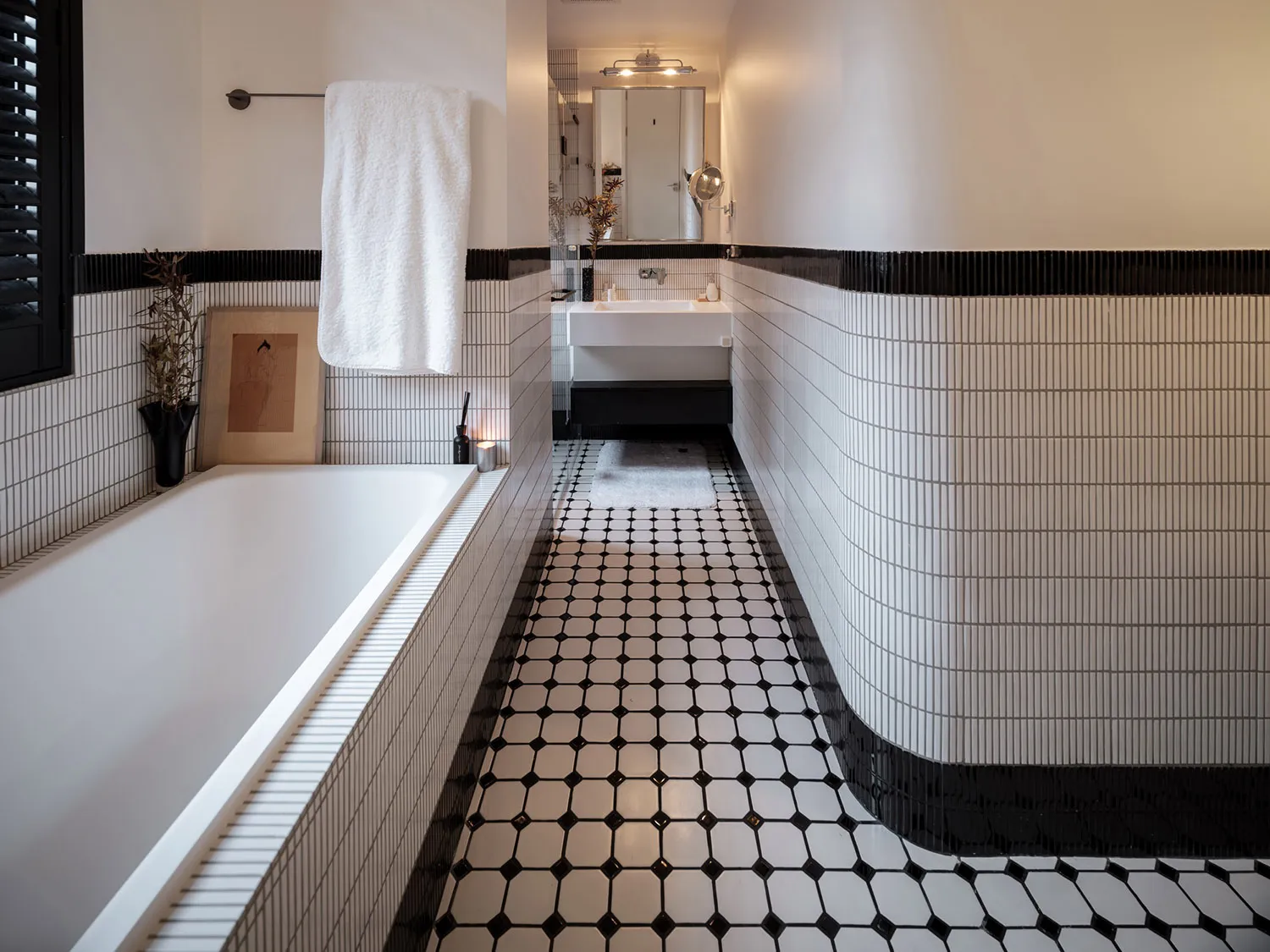 Minimalist bathroom with black and white tiled walls, white fixtures, and a white bathtub.