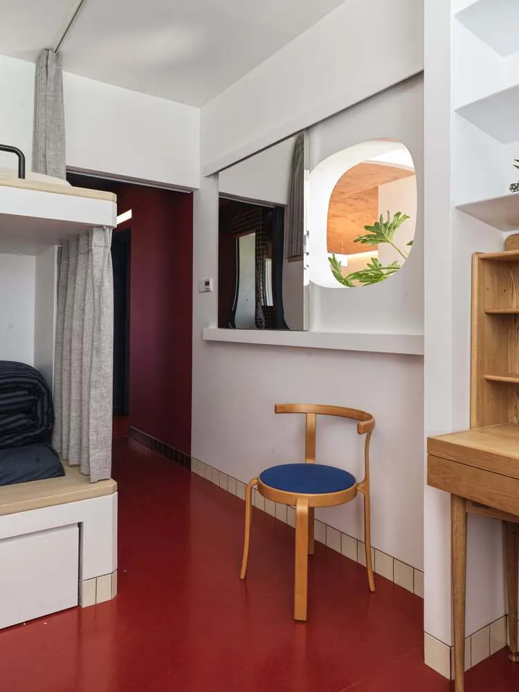 A minimalist living room with a red floor, featuring a blue cushioned chair and a wooden desk.