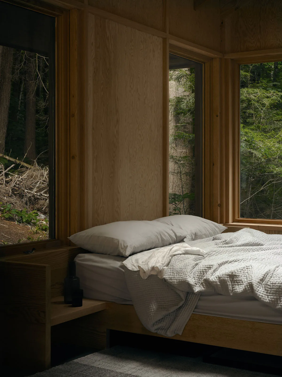 A modern bedroom featuring wooden furniture and a view of the forest through the windows.