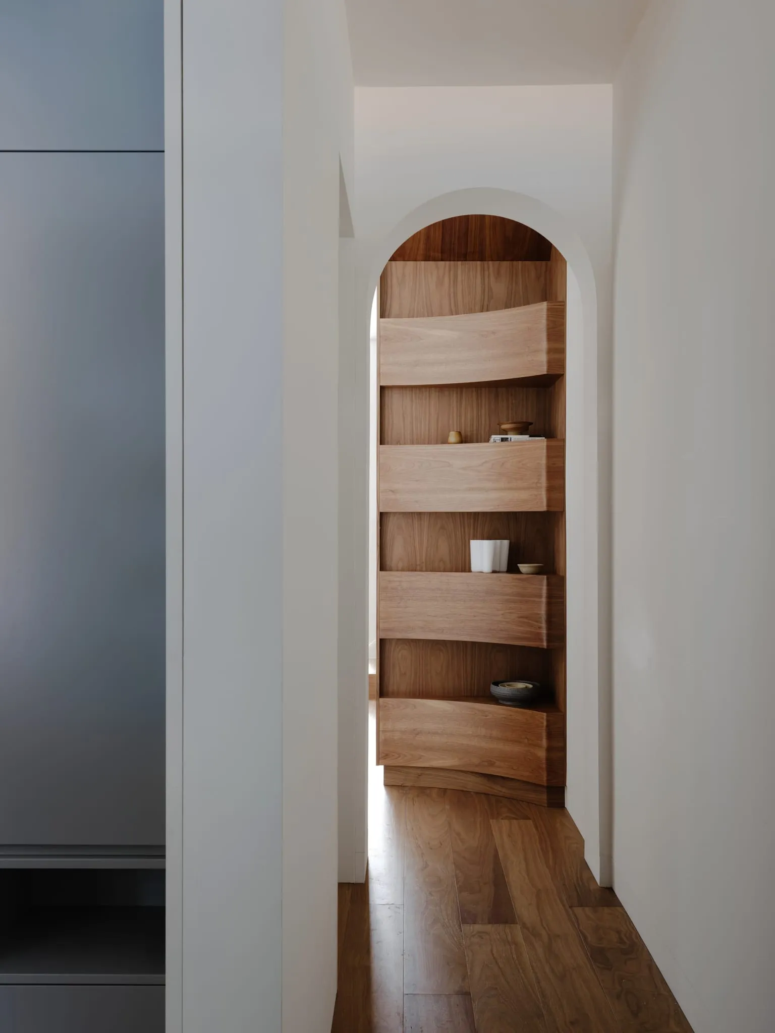 Modern minimalist wooden shelf with curved design and minimal objects.