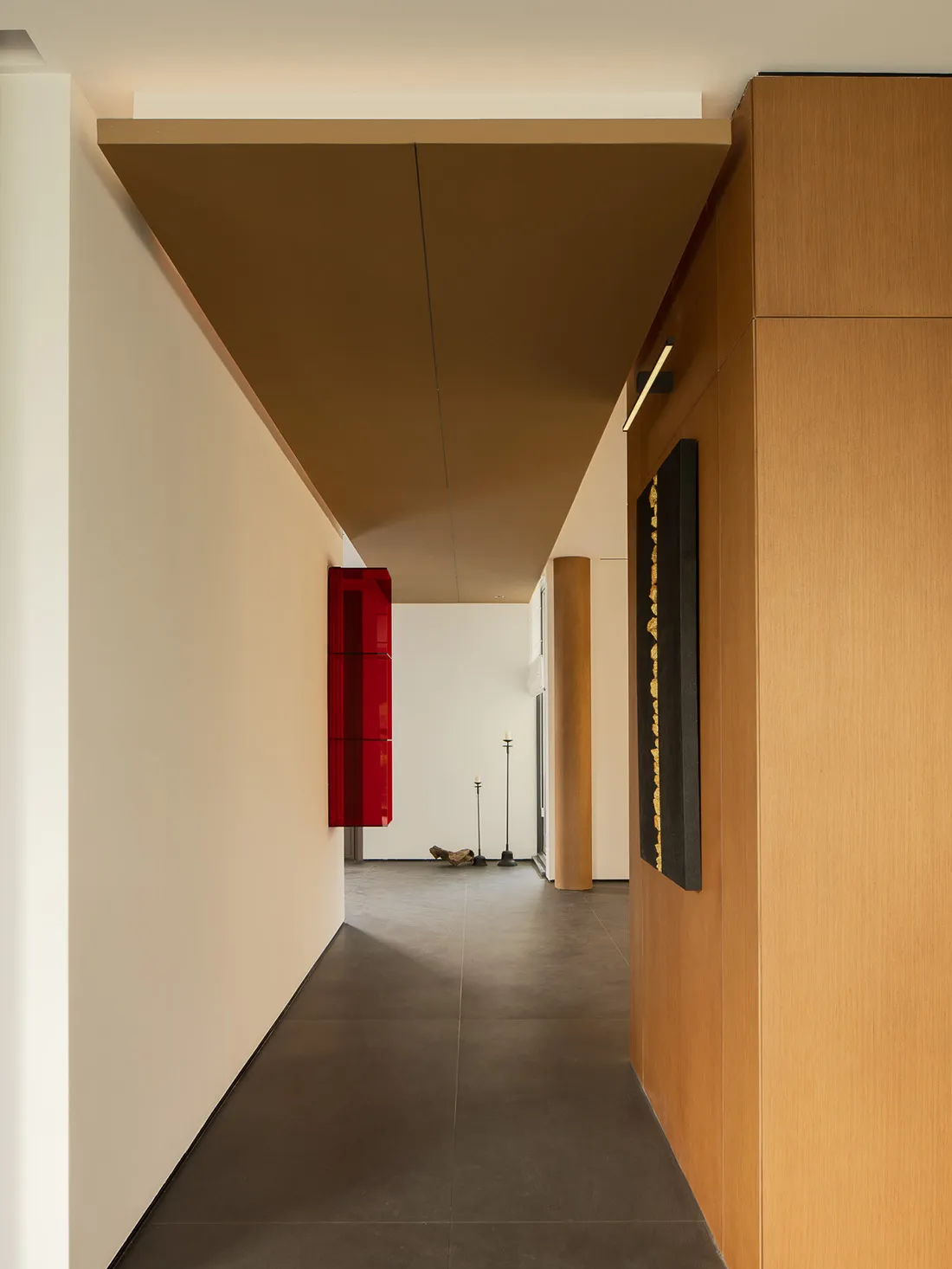 A minimalist hallway with steel and concrete finishes, featuring a wooden cabinet and a red window frame.