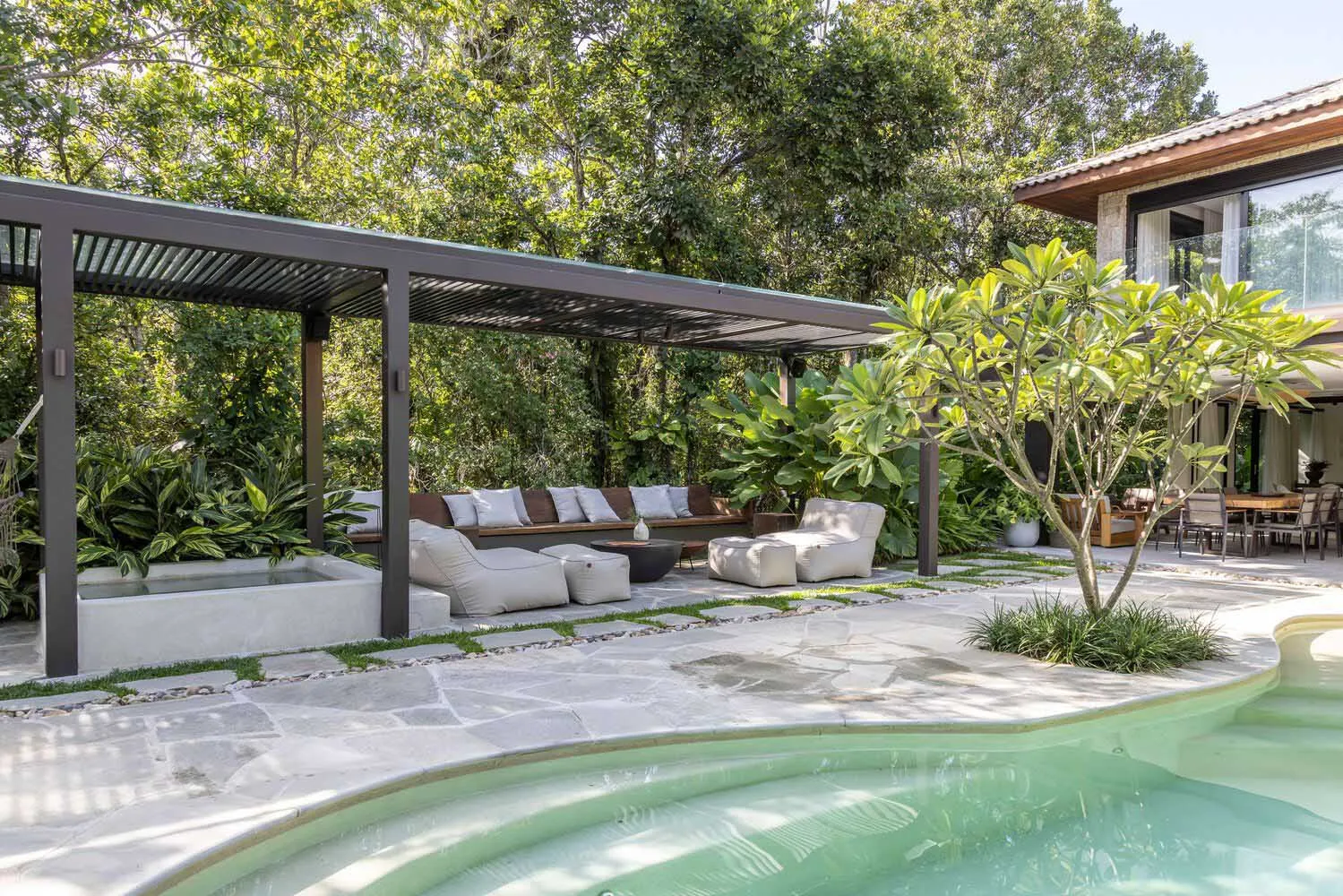 An outdoor living space featuring modern furniture, stone and concrete elements, surrounded by greenery.