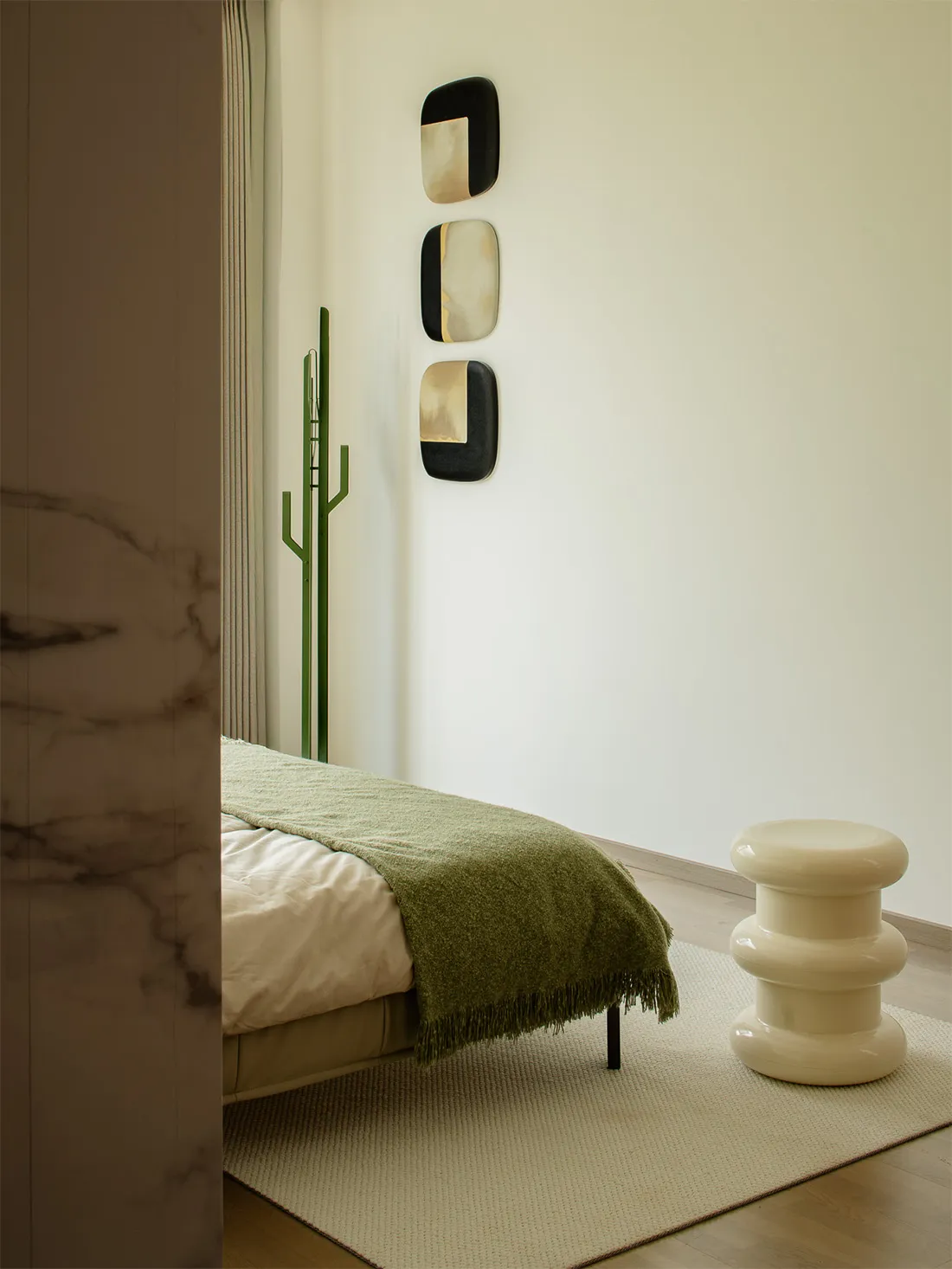 A minimalist bedroom featuring a green blanket, marble wall, and modern furniture.