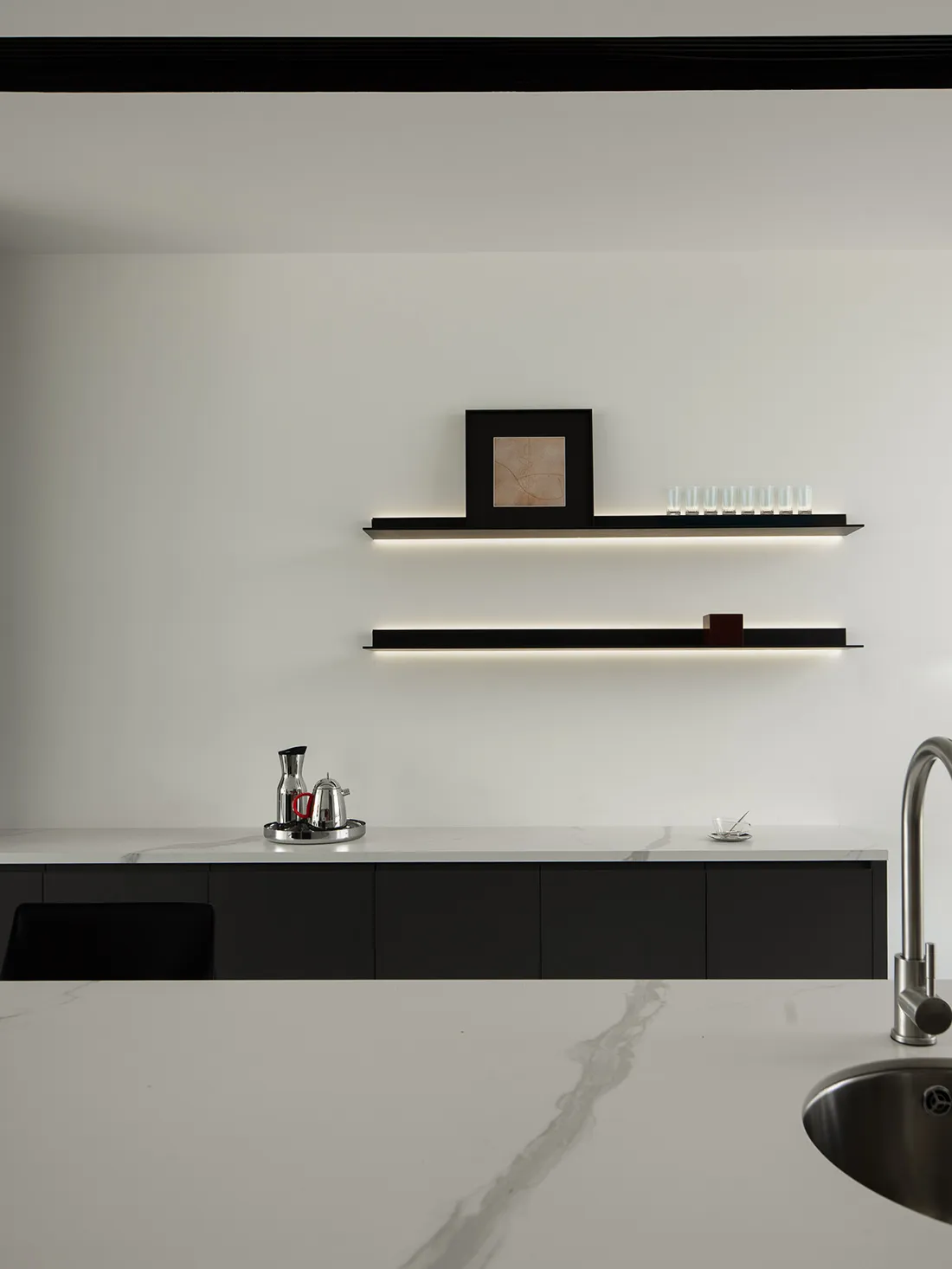 Modern minimalist kitchen with white marble countertops and black shelving.