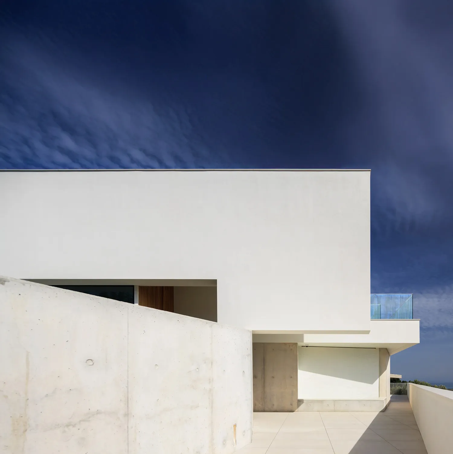 A minimalist, modern residential structure featuring white walls and a concrete patio.