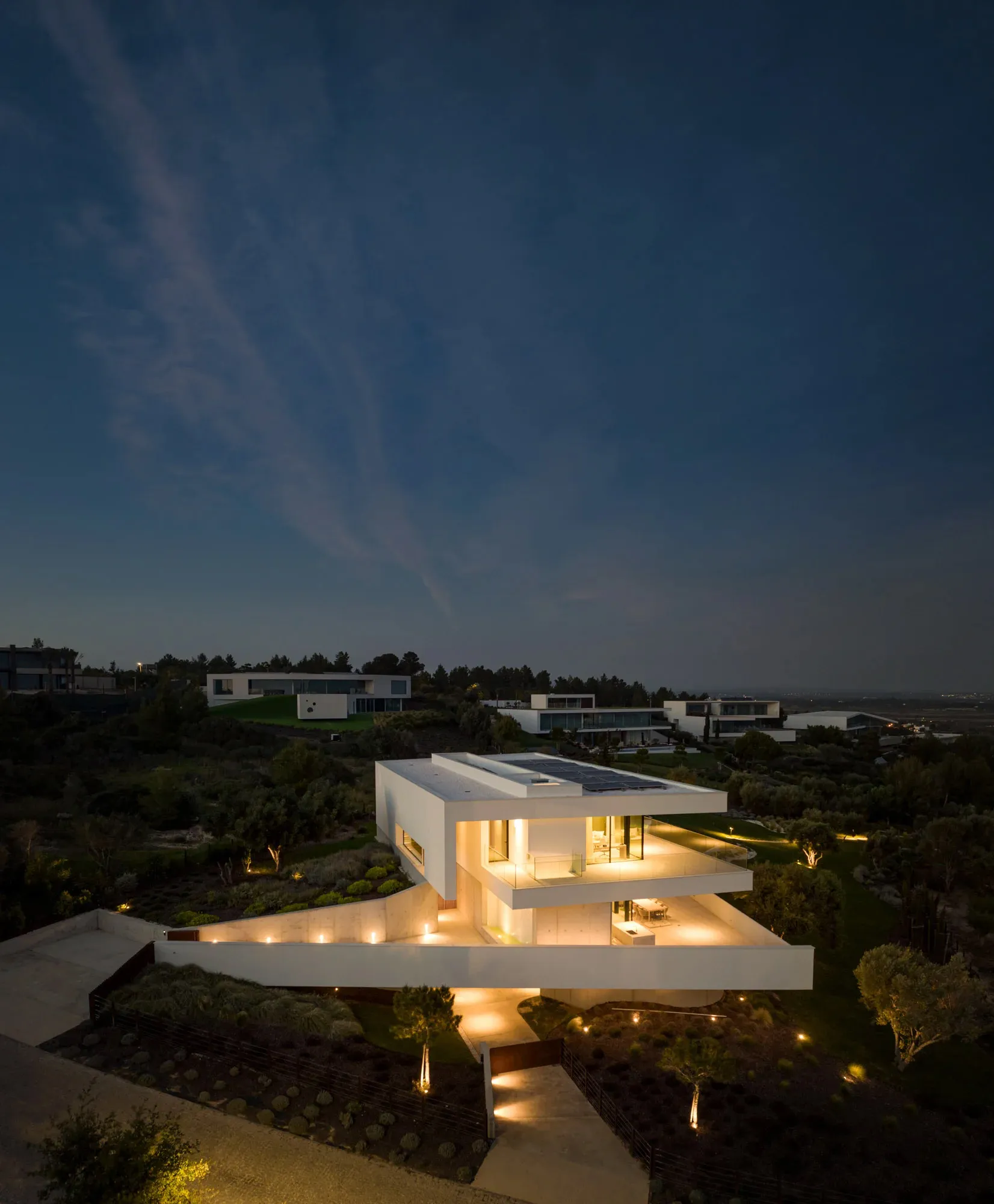 A modern house with concrete and glass exterior illuminated at night.