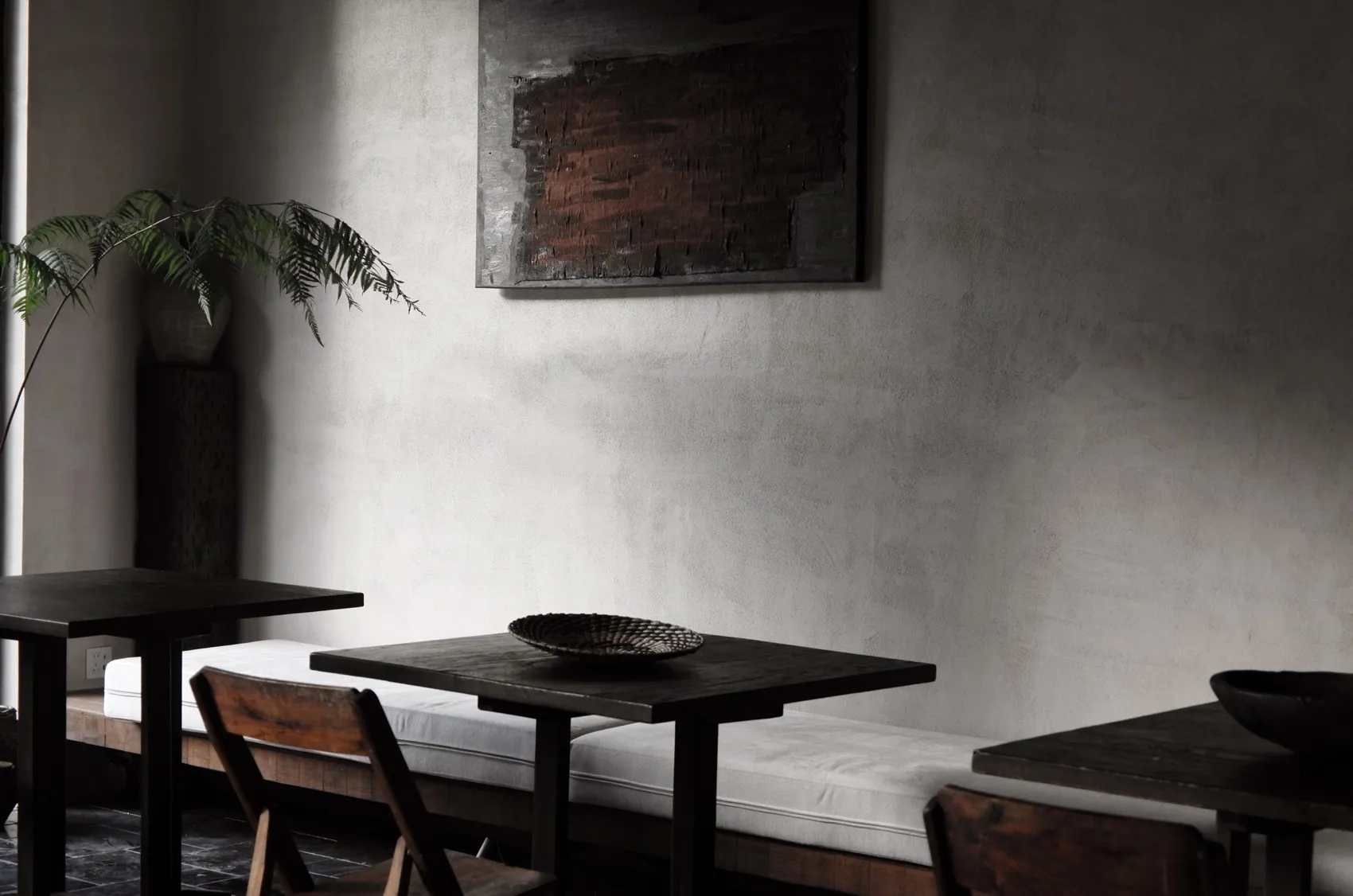 A minimalist restaurant interior featuring concrete walls and wooden furniture.