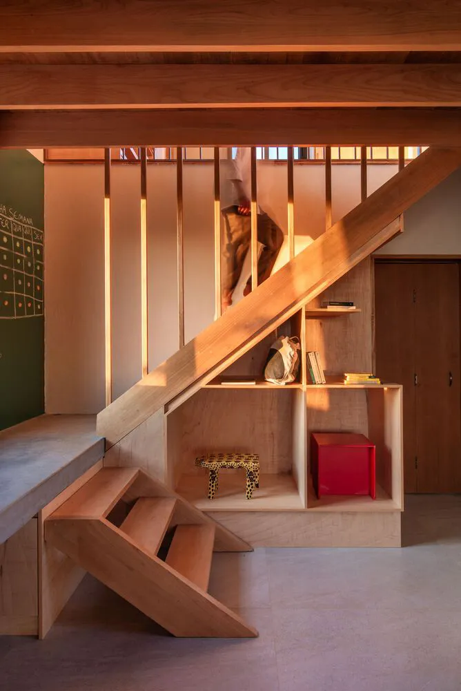 A modern interior featuring a wooden staircase with a built-in shelf containing books and decorative items.