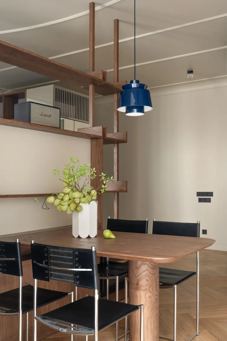A minimalist dining room featuring a wooden table with black chairs and a blue pendant light.