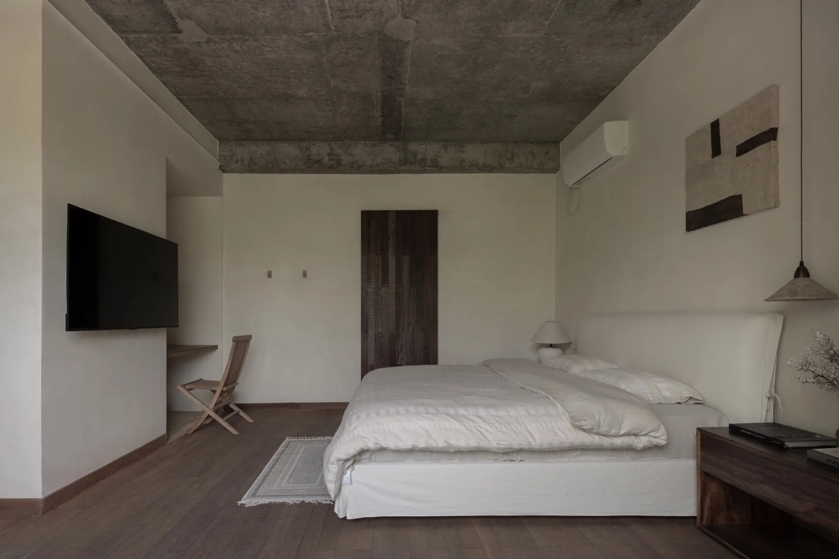 A modern industrial-style bedroom with concrete elements, featuring a single bed with white bedding and a minimalist design.
