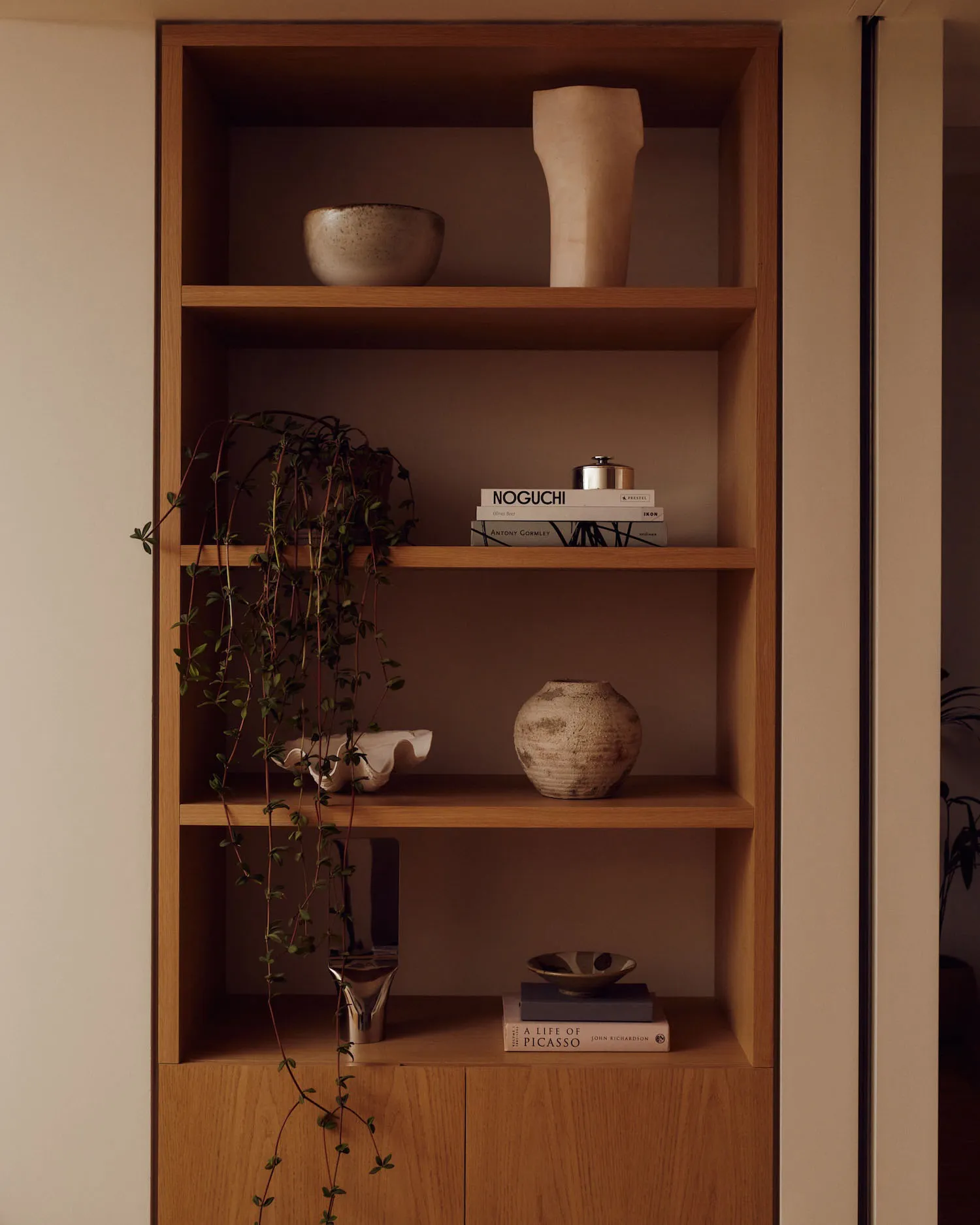 A modern home library featuring wooden shelving with a variety of decorative items, including books, vases, and a hanging pla