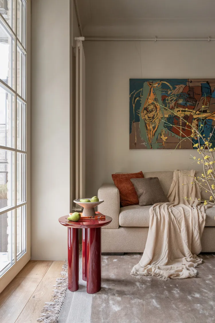 A modern living room featuring a contemporary art piece on the wall, a beige couch with cushions, and a red cylindrical table