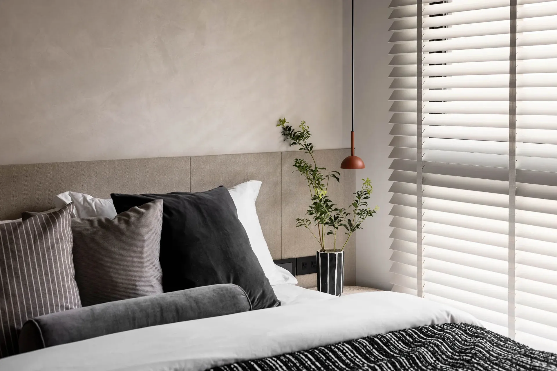 A neatly made bed with a modern minimalist design, featuring a wooden headboard, white bedding, and a green plant in a vase o