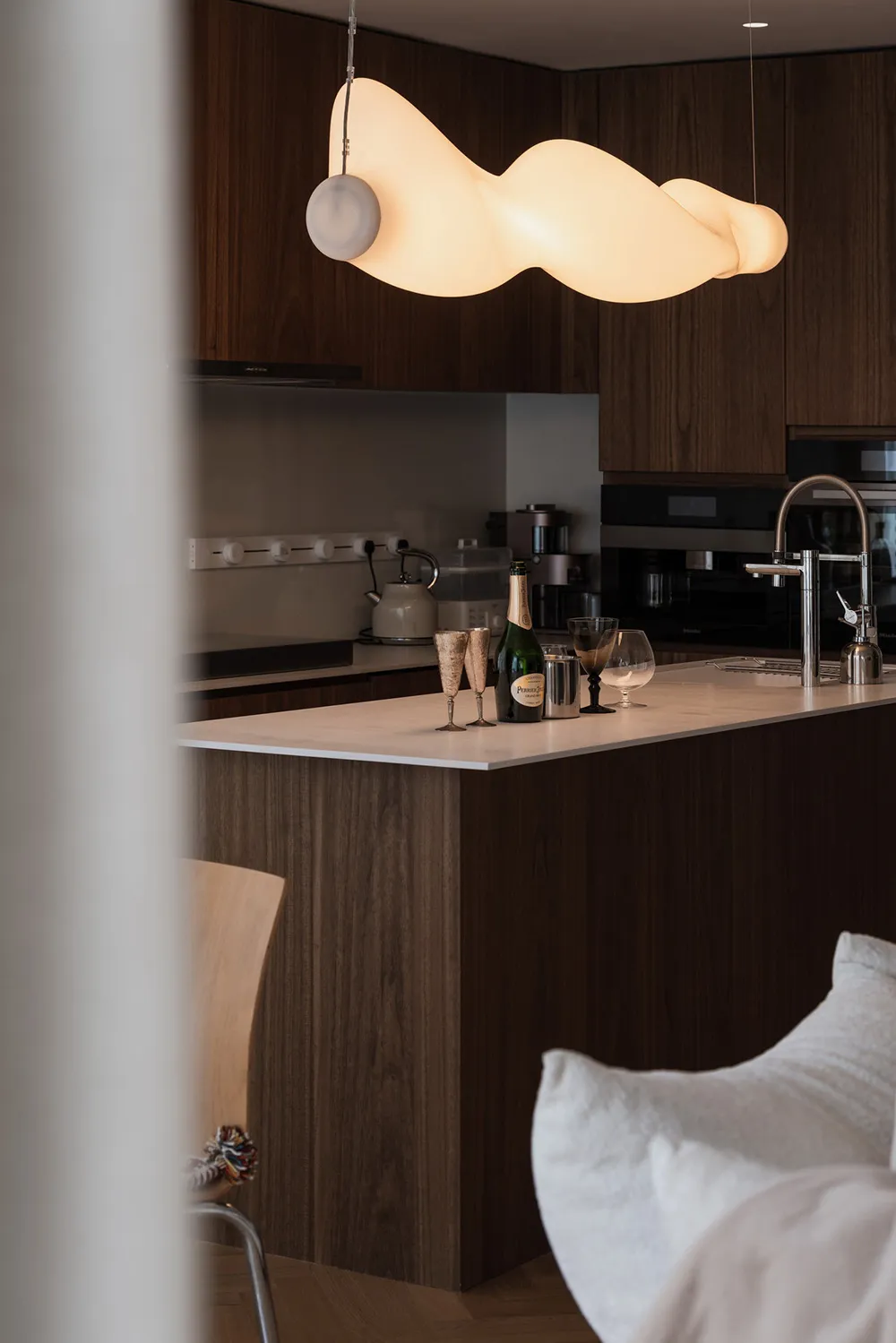 Modern kitchen with wooden finishes and a contemporary light fixture.