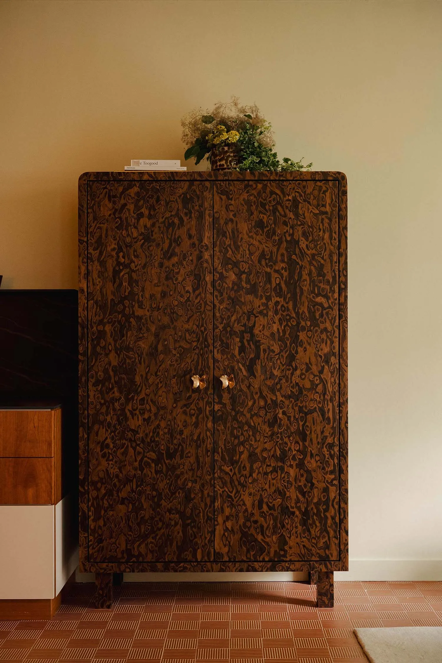 A modern living room with a wooden storage unit featuring two doors with gold handles, a vase of flowers on top, and a checke