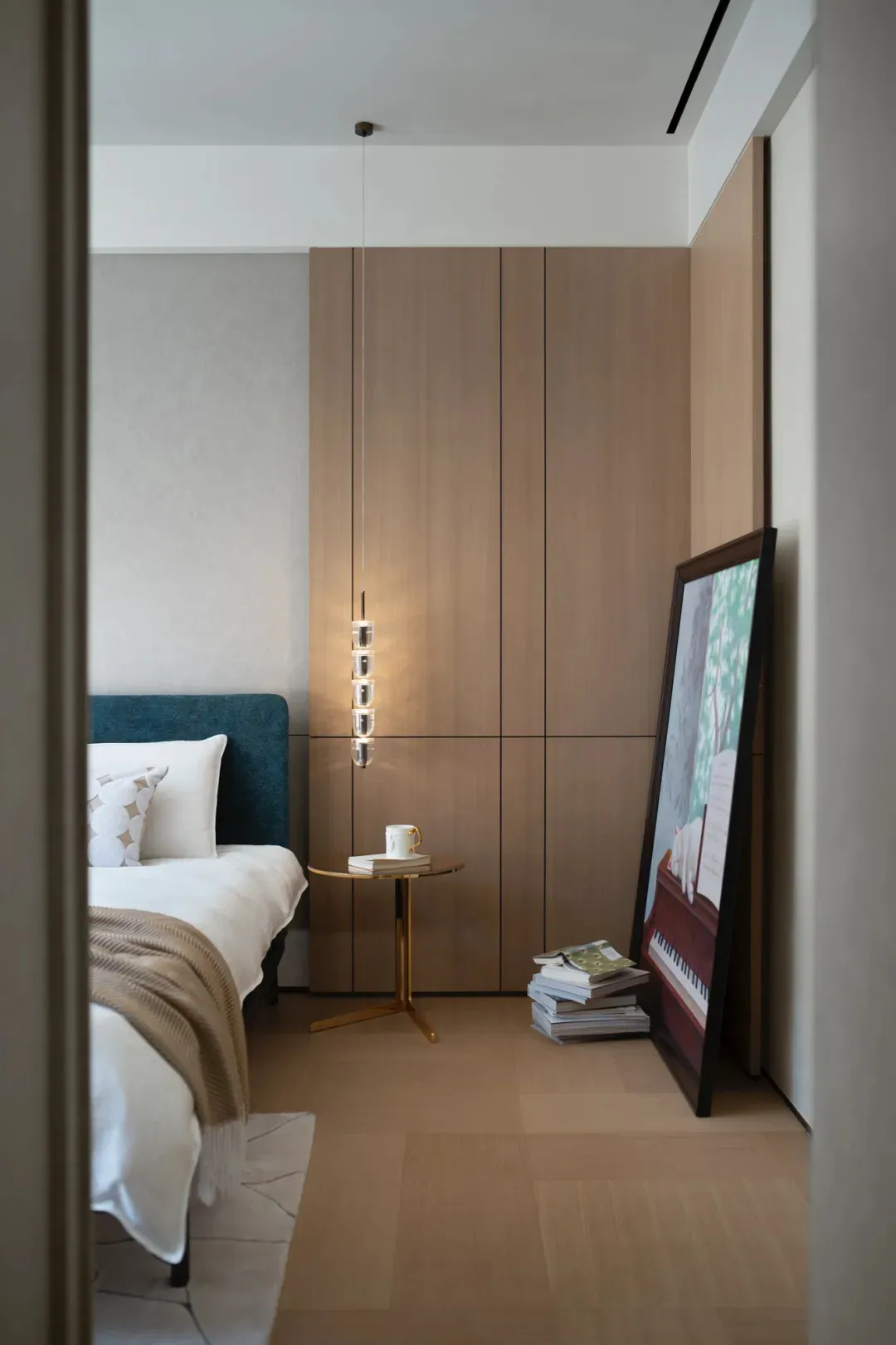Minimalist bedroom with a wooden cabinet, a cozy bed, and a small table with a cup and stack of books.