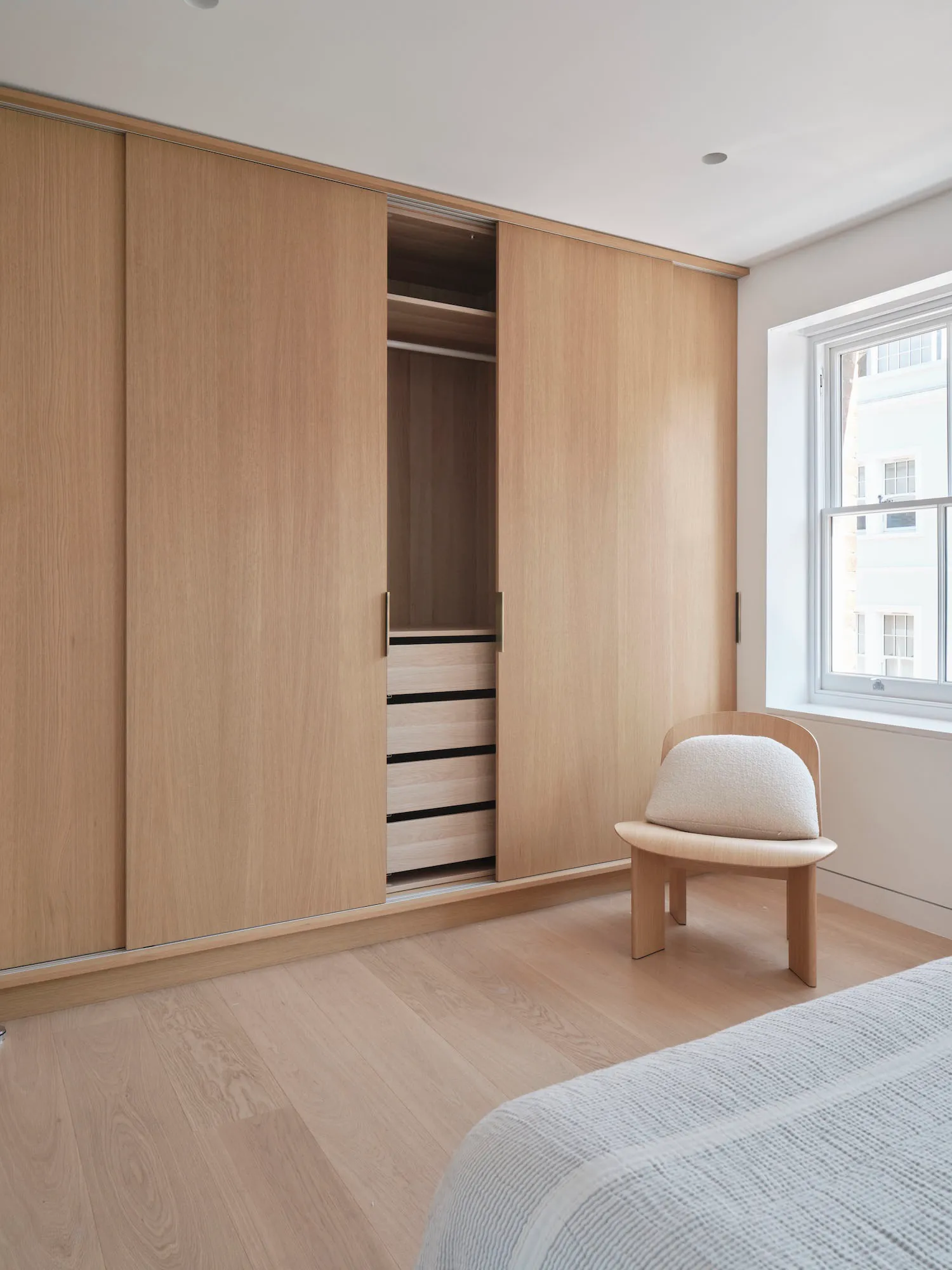 A minimalist bedroom featuring wooden cabinets with sliding doors and a white cushioned chair.