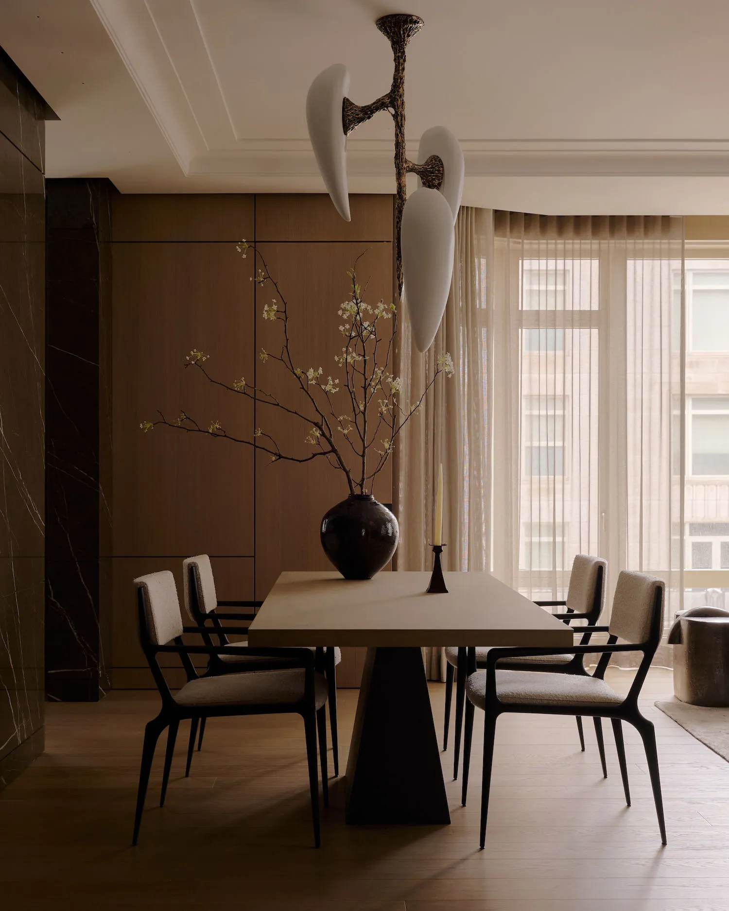 A modern dining room featuring wooden table, upholstered chairs, and metal pendant light.